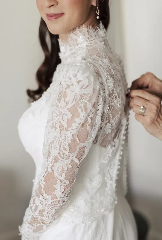 Bride buttoning lace sleeve on wedding dress during getting ready